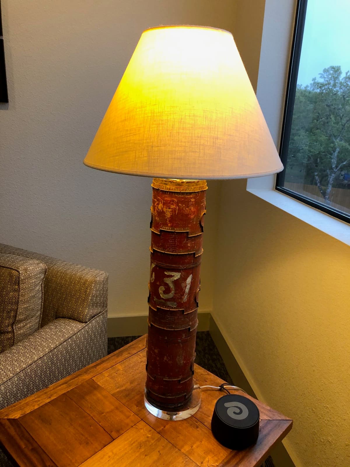 A lamp with a weathered red canister base on a wooden side table next to the sofa.