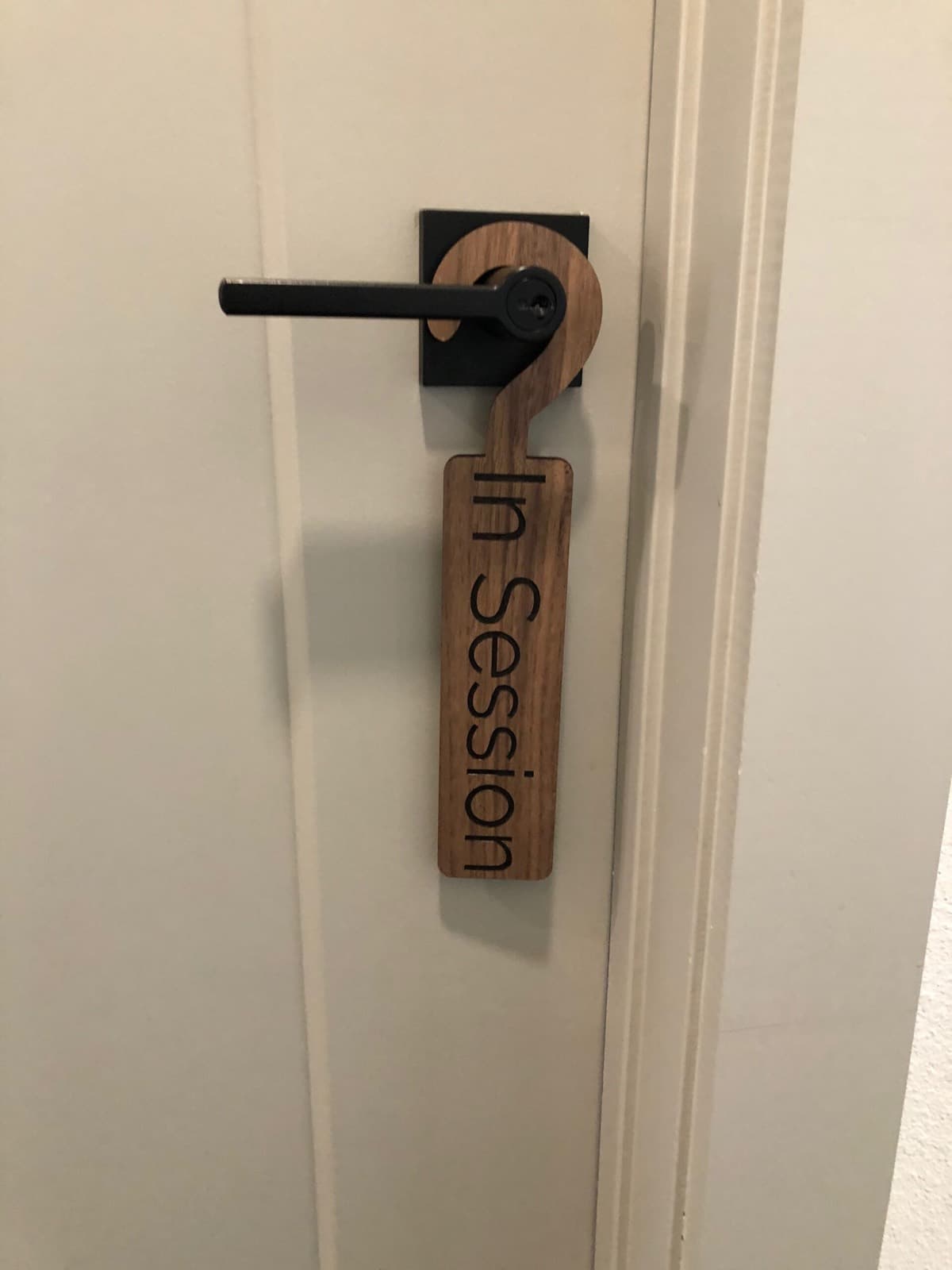 A wooden tag engraved In Session hanging from the office door handle.